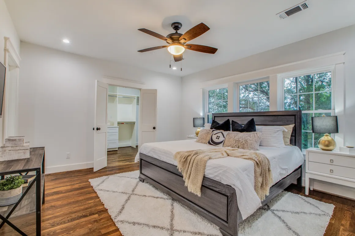 A bedroom with a bed, ceiling fan and hardwood floors.