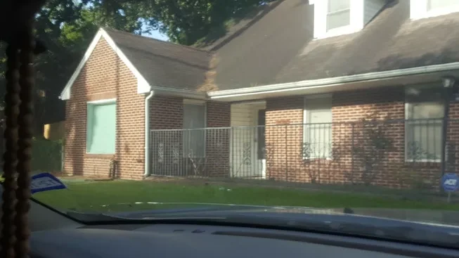 A car driving past a brick house with a fence.