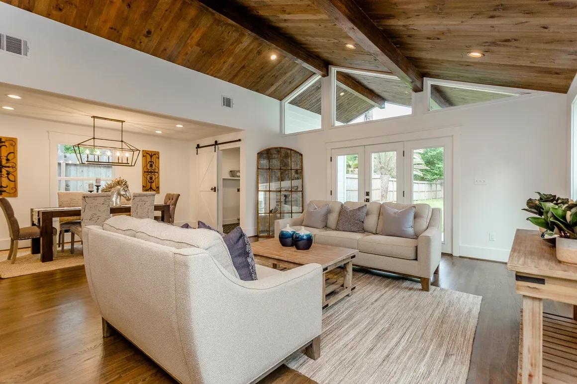 A living room with white couches and wooden ceiling beams.