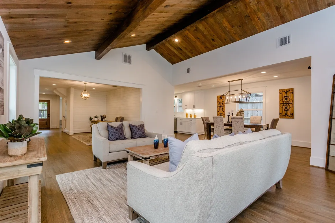 A living room with white couches and wooden ceiling beams.