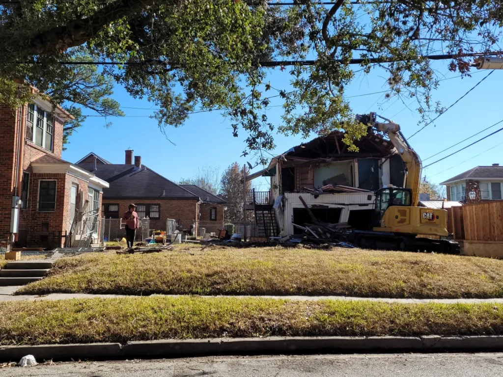 A house being demolished with a large yellow tractor.